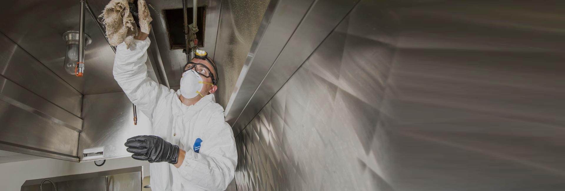 Cleaner in protective gear cleaning a commercial kitchen exhaust canopy
